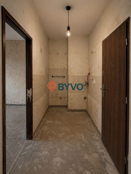 A spacious entrance area in a studio apartment with older tiles and lighting by a bulb.