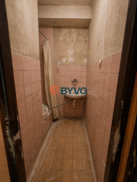 Bathroom in a studio apartment with old tiles and a narrow space for a shower.