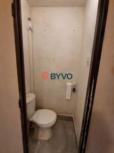 A toilet with prominent wall stains, gray floor, toilet paper holder.