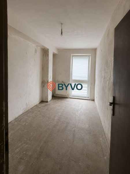 A view into an empty room in a two-room apartment with a concrete floor and balcony doors.