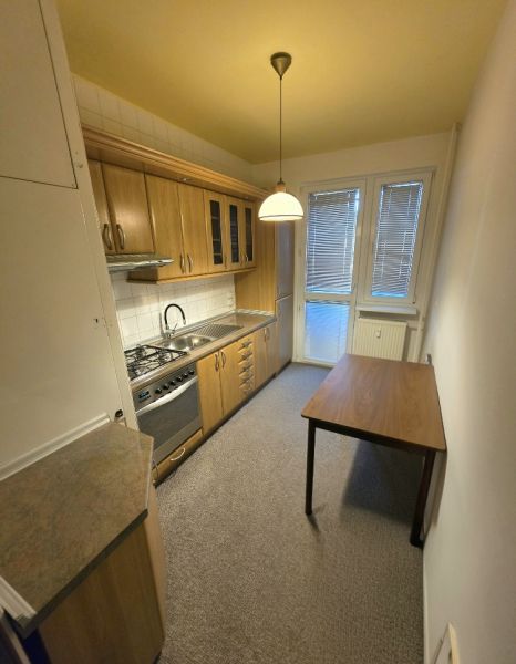 A kitchen in a 3-room apartment with wooden furniture, a dining table, and white lighting.