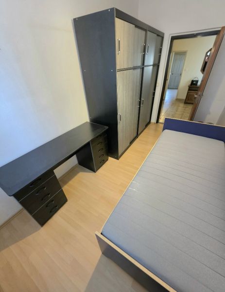 A bedroom in a three-room apartment with a wooden decor floor, a wardrobe, and a bed.