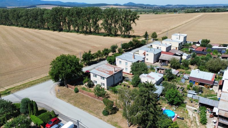 Family houses in Kráľovce on a street surrounded by fields and trees by the road.