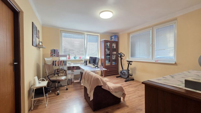 A room in a family house with a desk, wooden decor flooring, and an exercise bike.