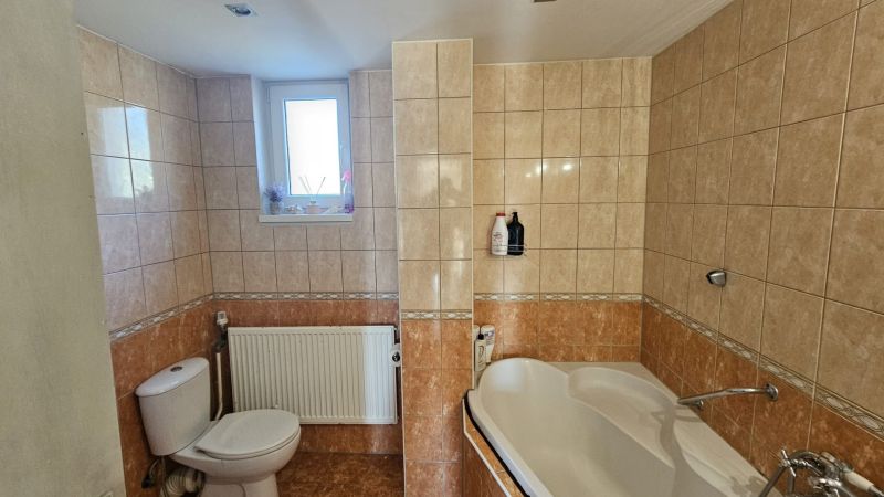 A bathroom in a family house with light tiles, a bathtub, and a window.