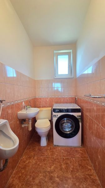 A bathroom in a family house with a washing machine, toilet, sink, and tiles in warm tones.