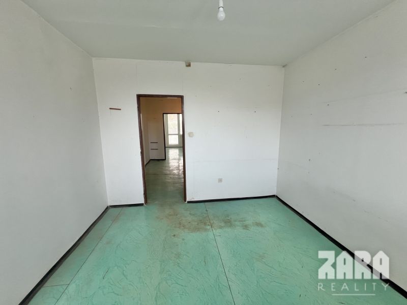 A room in a 3-room apartment with white walls and a colorful floor.