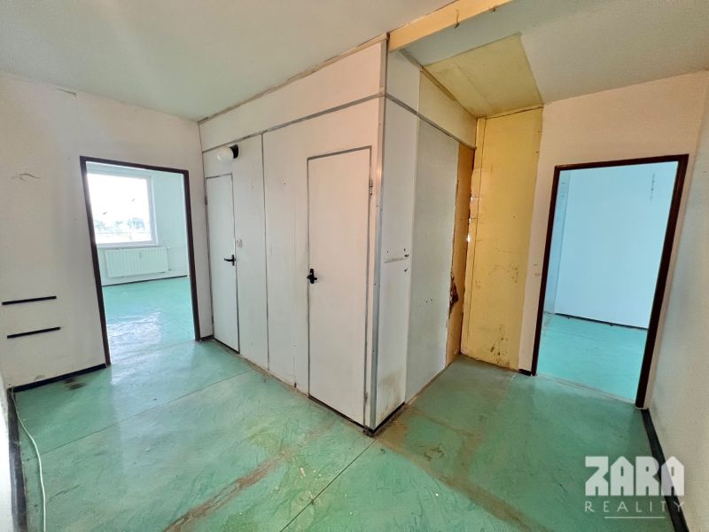 The interior of a 3-room apartment with white walls and a green floor in the hallway area.