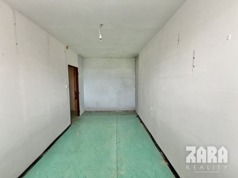 An empty room in a 3-bedroom apartment with a green base on the floor.
