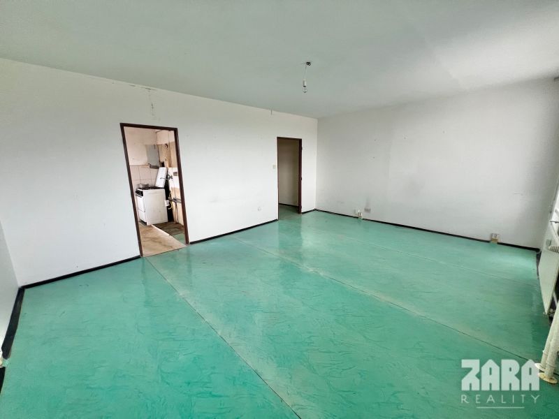 Empty room with a door to the kitchen, 3-room apartment. Green floor without decor.