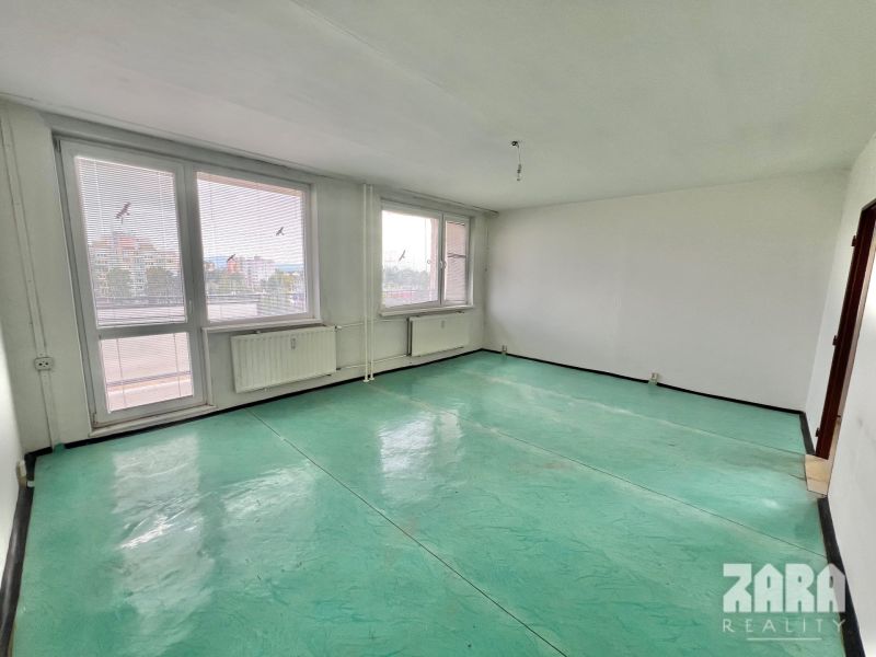 A spacious room in a 3-room apartment with large windows and a green floor.