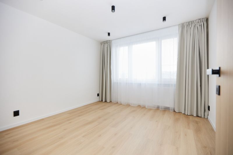An empty room with a window, curtains, and a wooden-patterned floor in a three-room apartment.