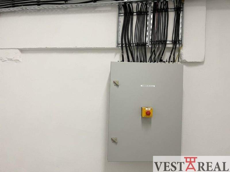 A distribution box in a warehouse and hall with numerous cables on the wall.