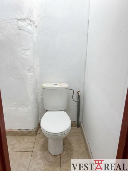 A toilet with white walls and ceramic tiles.