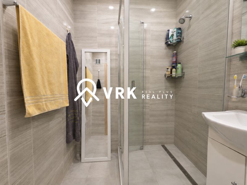 Bathroom in a studio apartment with a glass shower enclosure and light tiles.