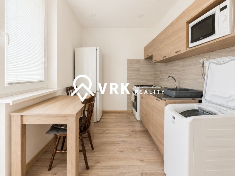 A kitchen in a studio apartment with a dark table and a light wooden-patterned floor.