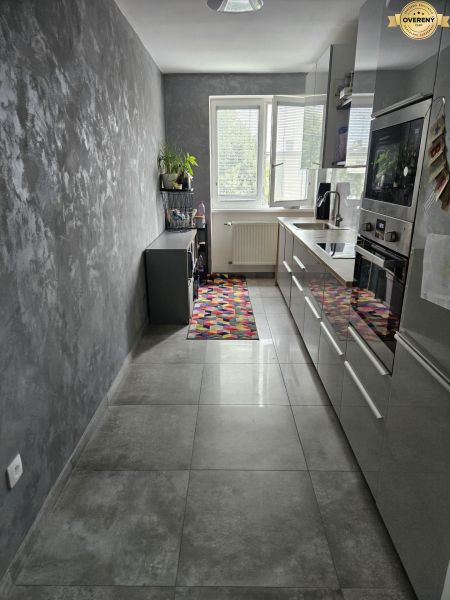 A kitchen with gray walls and flooring in a 4-room apartment, a colorful rug by the window.
