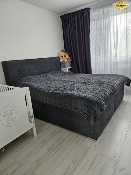 A bedroom in a 4-room apartment with a dark bed and a wooden decor floor.