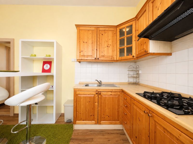 A kitchen in a studio apartment with wooden cabinets and a wooden-patterned floor.
