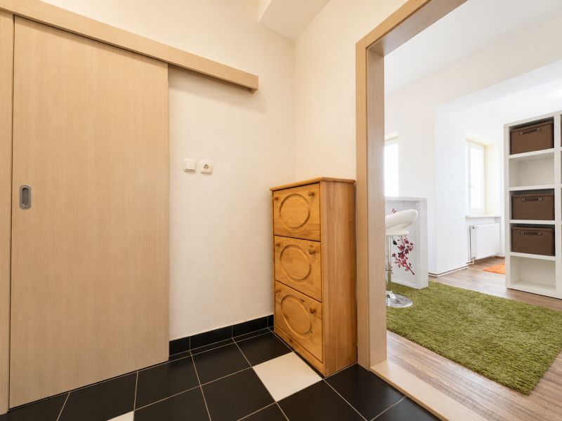 Hallway with a wooden chest of drawers, wooden-patterned floor, and green carpet.