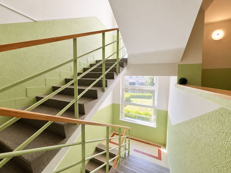 A bright stairway corridor with wooden railing and a view of greenery.