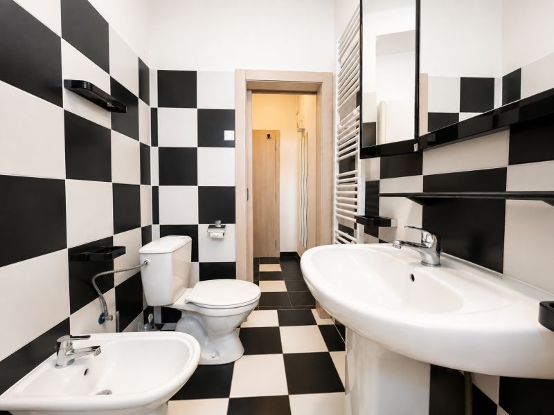 A bathroom with black and white tiles and ceramic sanitary equipment in a studio apartment.