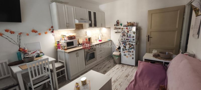 A kitchen in a studio apartment with white furniture and a wood-patterned floor.