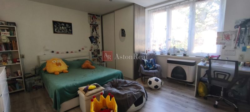 A bedroom in a studio apartment with a bed, a desk, and a wooden floor.