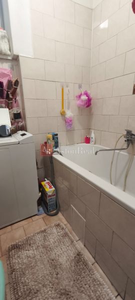 A bathroom with a bathtub in a studio apartment, equipped with a washing machine and cleaning supplies.