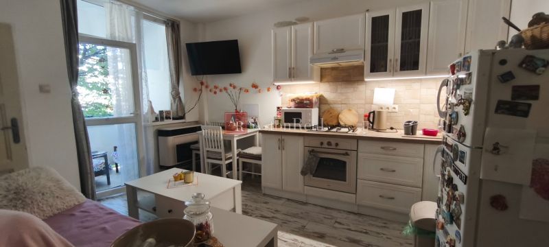 A kitchenette with white cabinets, a dining table, and a wooden decor floor in a studio apartment.