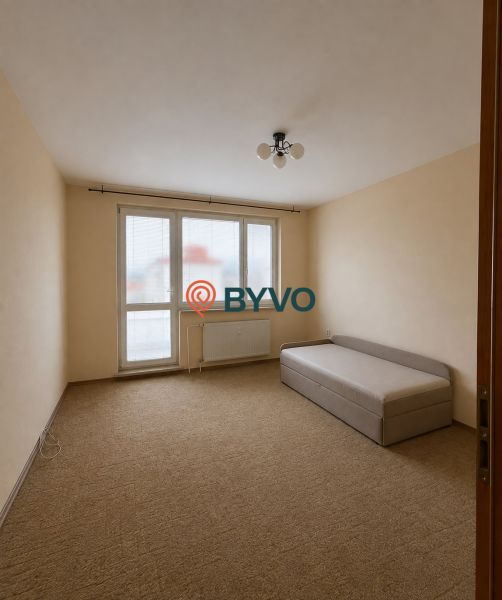A room in a 3-room apartment with a carpet and a simple bed, bright walls.