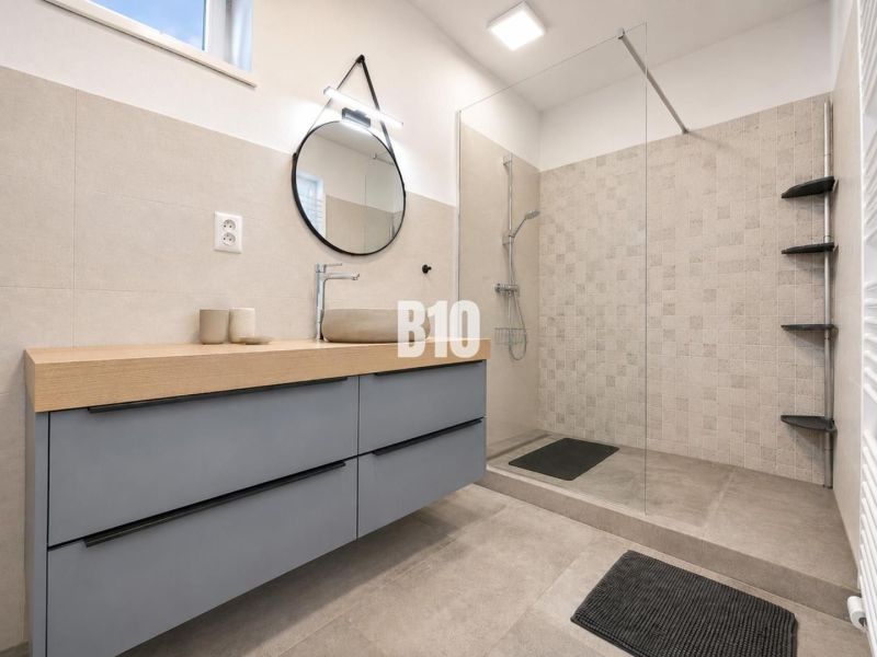 Interior of a holiday apartment with a modern bathroom, shower cabin, and round mirror.