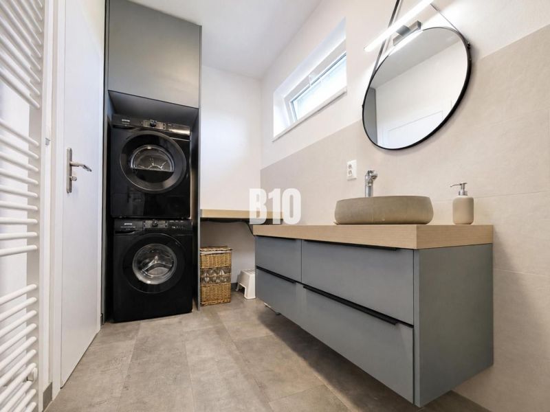 Bathroom in a holiday apartment with a washing machine, dryer, and wooden decor flooring.