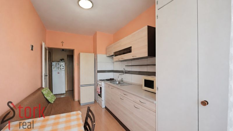 A kitchen with orange walls, cabinets, and white appliances in a 3-room apartment.