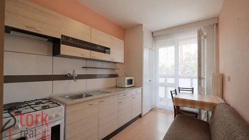A kitchen in a 3-room apartment with a wooden decor floor and balcony doors.