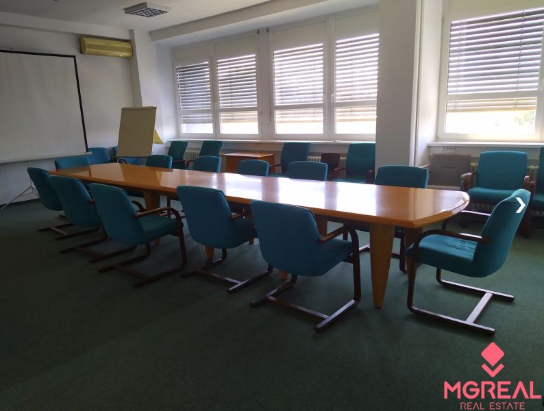 An office with a conference table and blue chairs on a carpet.