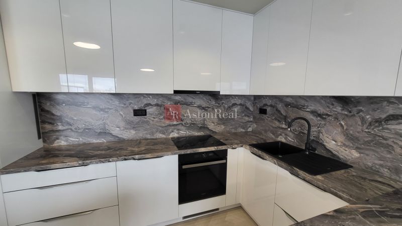 A kitchen with a sink and a stovetop; part of a 3-room apartment with a marble decor.