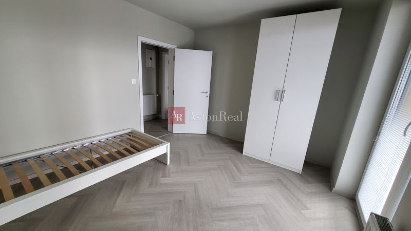 A bedroom in a 3-room apartment with a wooden decor floor, a bed, and a wardrobe.