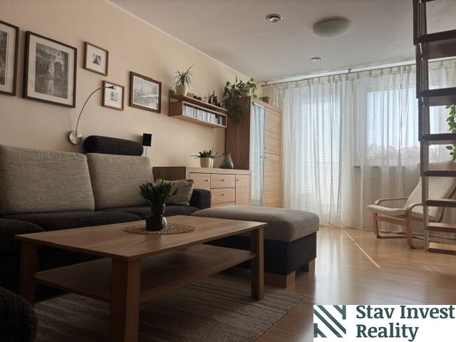 Living room in a 4-room apartment with a sofa, wooden decor flooring, and a staircase.