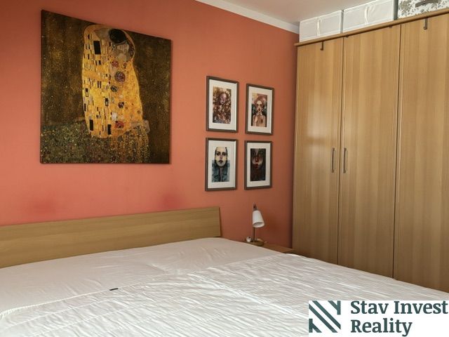 A bedroom in a 4-room apartment with an orange wall, paintings, and a wooden wardrobe.