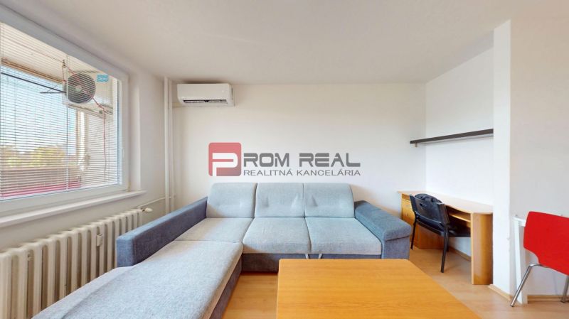 Living room with a sofa and a desk in a 3-room apartment with wood-patterned flooring.