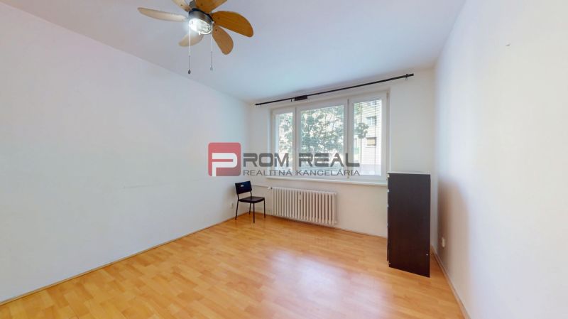 An empty room with a wooden-patterned floor and a large window in a 3-room apartment.
