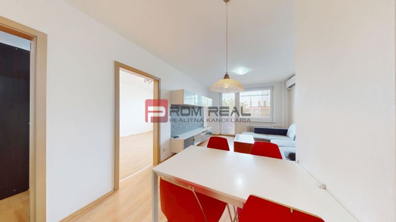 Dining area with a table and red chairs in a 3-room apartment, floor with wood decor.