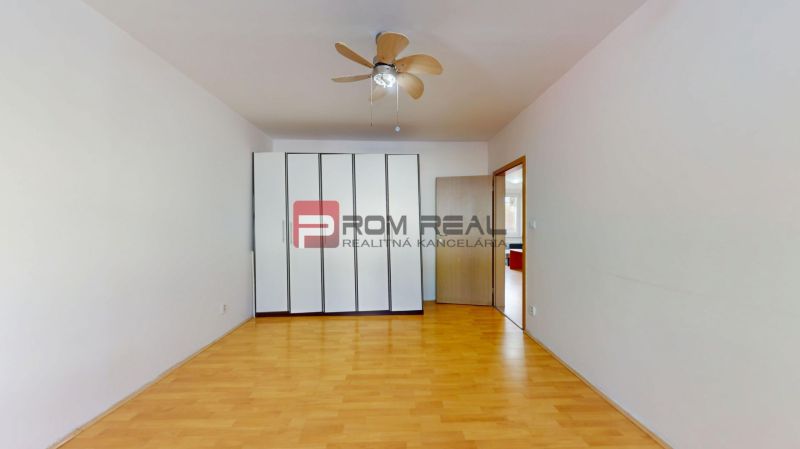 A room with a wooden floor decor in a 3-room apartment includes a built-in wardrobe and a fan.