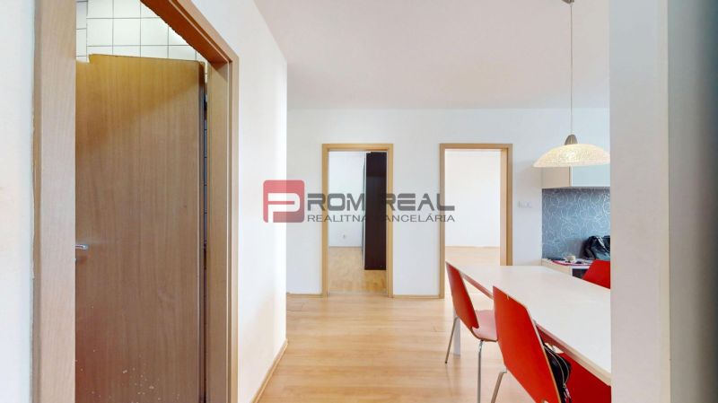 Interior of a 3-room apartment with a wooden decor floor, a table, and red chairs.