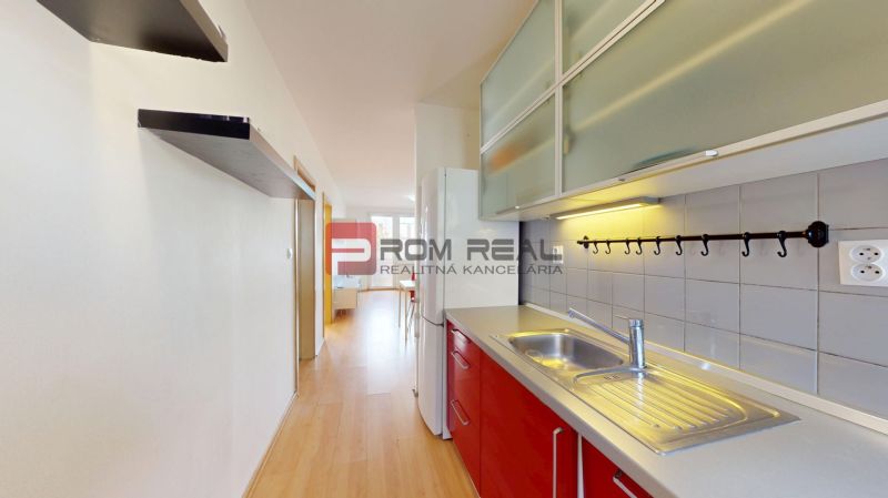 A kitchen in a 3-room apartment with a wooden decor floor and red cabinets.