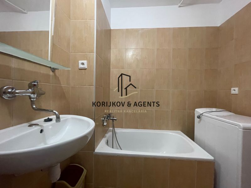 A bathroom with a bathtub, a sink, and a washing machine in a 2-room apartment.