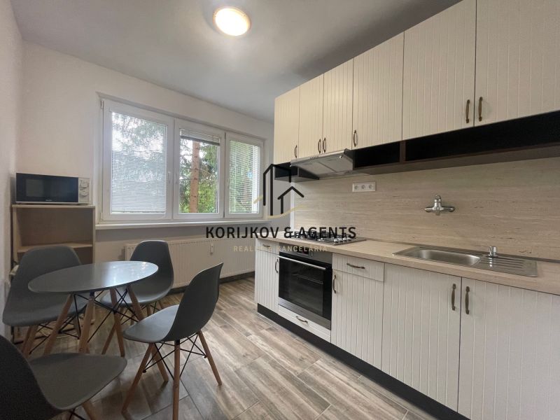 A kitchen in a 2-room apartment with a round table, four chairs, and a kitchen unit.