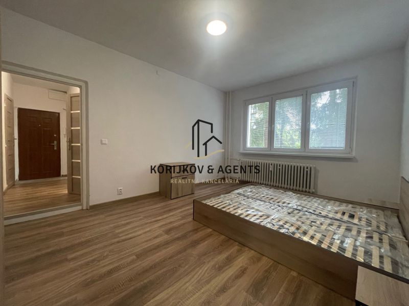 A bedroom in a 2-room apartment with a wood-patterned floor and large windows.