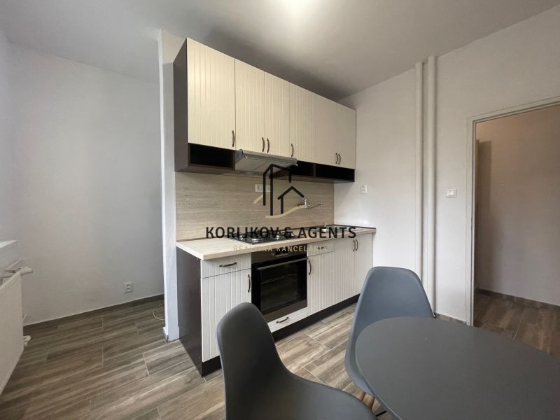 A kitchen in a two-room apartment with a wooden decor floor and a dining table.